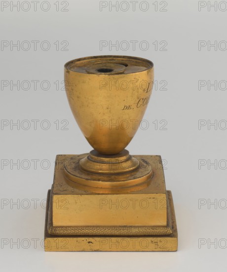 Inkwell, unknown creator; maker possibly Bylewski, Tadeusz 1866–1939; early 19th century, France ; inkwell; height 13.5 cm, width 9.4 cm, depth 8.4 cm, A gold-colored metal object with a rounded cup-like top that has a small central opening, mounted on a stepped circular base that sits on a rectangular pedestal; the surface shows a worn, slightly tarnished texture with darker spots and scratches, and the visible colors are gold, darker golden-brown patina, and a light gray background.