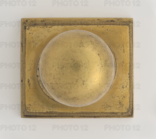 Inkwell, unknown creator; maker: Bylewski, Tadeusz 1866–1939; early 19th century, France ; inkwell; height 13.5 cm, width 9.4 cm, depth 8.4 cm, A square metallic object with a raised circular dome in the center, showing a worn, scratched surface and a decorative braided border, primarily in shades of gold with areas of darker tarnish and black spotting, set against a light off-white background.