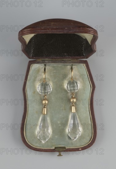 Pair of earrings in a leather case. Made by Sazikov goldsmith's firm; 1793–1887. Pair of earrings made of 56 gold with a faceted rock crystal teardrop set in gold and suspended from a faceted crystal ball. 19th century, St. Petersburg, Russia. Jewelry., An open brown case with a hinged lid reveals a pale green velvety interior holding a pair of dangling earrings; the lid interior shows dark brown textured lining and light beige corners, and the case edges are dark brown with a small brass clasp. The earrings feature faceted clear round beads, small gold-toned spherical elements and tapered gold-toned fittings above faceted clear teardrop pendants, all set against the pale green background. The visible colors include brown, pale green, dark brown, beige, gold, and clear.