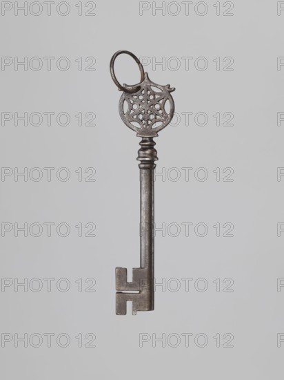 Key, locksmithing, rosette ornament. A key of the so-called Venetian type with a smooth tubular shaft and a feather extending below the shaft; lower edge widened on one side. Turned, profiled knot; circular handle with an inscribed six-pointed rosette with circles between the radii. The form of the knot is not found in other keys from that period. Perhaps 19th century, 17th century, unknown locality, locksmithing., A single ornate metal key is shown against a plain light gray background, with a round decorative bow featuring a filigree pattern and a small attached ring, a cylindrical stem with a few ridged bands near the top, and a notched bit at the bottom; visible colors include shades of metallic gray and silver and the light gray of the background.