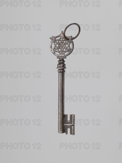 Key, locksmithing, rosette ornament. A Venetian-type key with a smooth tubular shaft, a feather extending below the shaft, and a lower edge widened on one side. Turned, profiled knot; circular handle with an inscribed six-pointed rosette with circles between the radii. Knot form not found in other keys from that period. Perhaps 19th century 17th century?. Unknown locality., A single metal key is shown against a light gray background, with a round ornate bow featuring a circular filigree pattern and a small ring attached, a long cylindrical shaft with a stepped collar near the top, and a rectangular bit with symmetrical protrusions; visible colors include shades of gray, silver, and dark metallic tones.