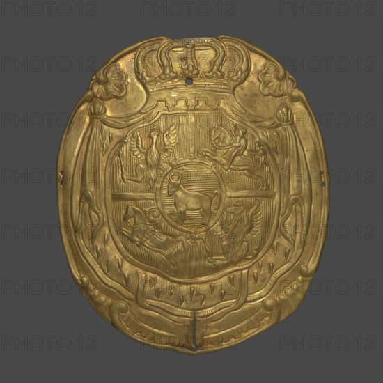 A plate for a patrontasz cargo bag with the Ciolek coat of arms and the coat of arms of the Polish-Lithuanian Commonwealth, 18th century, Poland; materia/varia; height 16 cm, width 14 cm, depth 2.3 cm; coats of arms, weaponry., A rounded ornamental plaque with a metallic gold surface against a solid dark gray background, featuring an embossed central shield topped by a decorative crown and surrounded by draped ribbon-like motifs; the shield contains a circular central medallion with a relief of a four-legged animal, flanked in the shield's quarters by a pair of winged bird figures and a pair of horse-and-rider figures, all rendered in raised, textured relief, with ornamental flourishes and small punched holes visible near the plaque's edges.