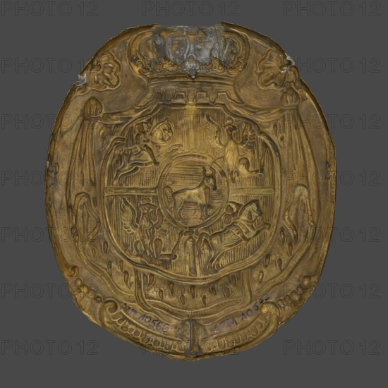 A plate for a patrontasz cargo bag with the Ciolek coat of arms and the coat of arms of the Polish–Lithuanian Commonwealth, 18th century, Poland; coats of arms; weaponry; varia; height 16 cm, width 14 cm, depth 2.3 cm;, A worn, oval metal plaque with a raised, ornate central design in shades of gold and brown sitting against a gray background; the plaque shows a circular central medallion containing an animal figure surrounded by carved borders and decorative motifs including winged and equine figures, flowing drapery-like shapes, and scrollwork, with areas of darker tarnish and small patches of grayish corrosion near the top and along the edges, and subtle greenish-blue spots in a few places.