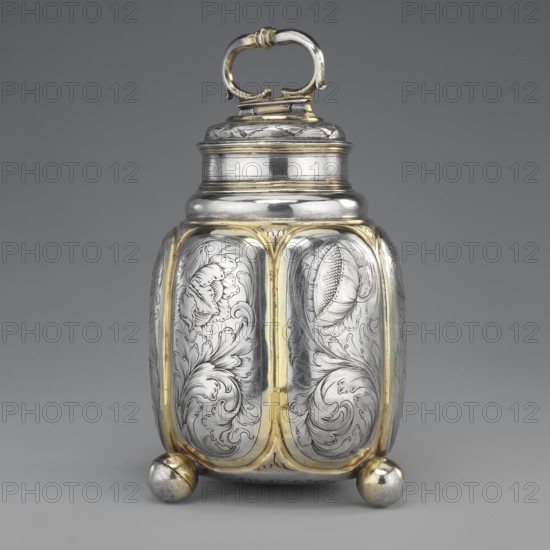 Flasza, Jachman, Hans young; fl. 1681–1728 goldsmith; plant decoration; Baroque; flowers. Oval box supported by three balls with a cylindrical, threaded lid with an oval profiled handle on a hinge. On the body are six repoussé oval vertical reserves with engraved plant-floral volutes. The balls, reserve edges, and interior are gilded. Late 17th century; Wroclaw, Silesia. Vessel; height 16.5 cm, width 10.5 cm., A metallic container with a rounded rectangular body standing on a group of rounded feet, featuring ornate engraved floral and foliate patterns on its panels and a hinged lid with a looped handle; the surface shows polished silver tones with highlights of warm gold accents along the panel edges and feet, and the background is a neutral gray.