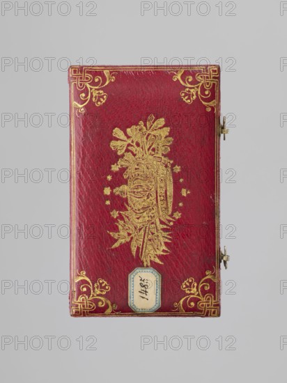 Rectangular key case with a hinged lid and two clasp hooks. Trimmed with red leather, with gilded embossing; on the lid a frame along the edge with an ornament in the corners. In the centre, a ducal mitre. On the underside, a gilded frame along the edge; in the centre a non-gilded embossed rhombus with an inscribed quatrefoil, and in the centre a rhombus with a four-petal rosette. Glued on a printed card and with a typewritten note describing that it was presented in 1833 as a wedding gift. 1833, Darmstadt, Germany; materiaI/varia. Dimensions: height 9.8 cm, width 5.9 cm, depth 1.8 cm., A rectangular book cover in a deep red color with ornate gold decorative corners and a central gold embossed motif, a small metal clasp on the right edge, a small pale blue and cream label near the bottom center, and a neutral light gray background.