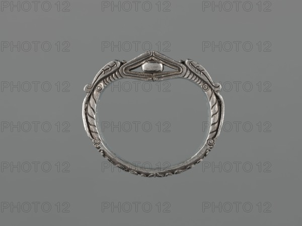 Bracelet;, scrap-purchase provenance; Chinese/Mongolian; 19th century, China, Mongolia ; materials: metal jewelry; design: dragons, dragon with pearl, hundred antiquities baigu ornament; function: body/hand ornament, fashion accessory; dimensions: height 8.0 cm, width 9.0 cm, weight 281 g., A metallic circular bracelet with ornate carved details forming a symmetrical design, showing leaf-like motifs and curved ridges around its band; a raised decorative element sits at the top center within a triangular frame. The object appears in shades of silver and gray against a uniform gray background.
