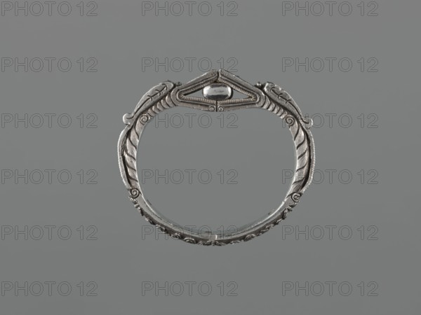 Bracelet, scrap-purchase provenance; Chinese/Mongolian body ornament hand ornament, jewelry, 19th century ; dragon with pearl motif; hundred antiquities baigu ornament; materials not specified; height 8.0 cm, width 9.0 cm, weight 281 g., A circular metallic bracelet with ornate carved detailing sits centered against a plain gray background; the metal appears silver with darker gray patina in recessed areas, featuring symmetrical leaf-like motifs and curved ridges along the band, a raised central decorative element at the top with a smooth oval bead, and fine linear textures and scrollwork around the edges, all shown in shades of silver and gray.