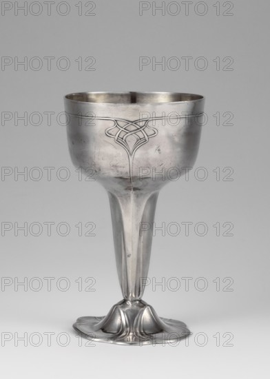 Art Nouveau silver cup, Orivit AG Cologne; goldsmith's manufactory; 1894–1905; 1906–1914 after takeover by WMF; Art Nouveau style. Supported on a flower-shaped foot. Tall stem widening toward the top to a hemispherical bowl with a slightly flattened bottom, decorated with a geometric-floral ornament. Dated 1906–1914, Cologne, Germany. Vessel. Height 12.1 cm, width 7.1 cm, weight 125 g., A single metallic goblet shown against a plain light gray background, with a smooth rounded cup and a long tapering stem that flares into an ornate, organic-shaped base; the goblet surface is reflective silver with visible scratches and subtle darker tarnish areas, and there is a raised decorative knot-like motif on the upper part of the cup; overall colors visible are silver-gray and light gray with small darker gray accents.
