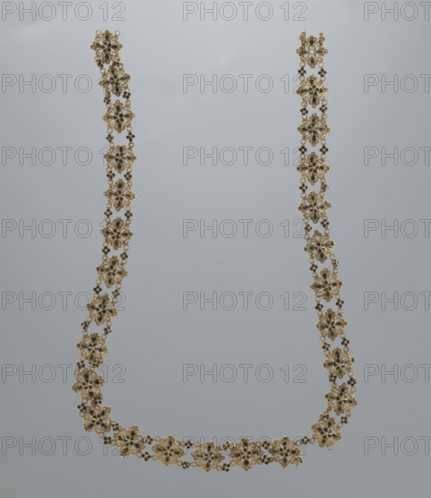 Necklace, rosette motif, jewelry, women's accessory, mid-19th century, Italy, weight 16.57 g, length 37.5 cm, A delicate floral necklace suspended against a neutral gray background, composed of a repeating pattern of ornate flower-shaped links with filigree details, small round bead accents, and tiny connecting chains; the piece shows metallic gold tones with dark accents and subtle reflective highlights, forming a U-shaped drape with a few slight bends where it hangs.