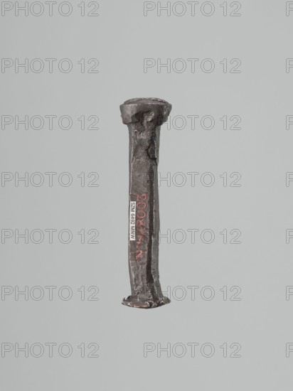 Stamp - die, Szewczykowski, Roman 1849–1901 — gift; locksmithing. Oval convex stamp-die with a depiction of the king's bust in an open crown. Origin uncertain; possibly Poland; 18th or 19th century. Die: height 9.5 cm, width 2.3 cm, depth 1.8 cm., A single vertical metal object with a rough, irregular surface and a flattened head and foot, shown against a plain light gray background, with colors including dark gray, rust-brown, black, and hints of red.