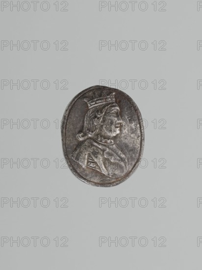 Stamp-die, Roman Szewczykowski 1849–1901 noted; locksmithing. Oval convex die with depiction of a king's bust wearing an open crown. Origin uncertain; possibly Poland; dated 18th or 19th century. Die dimensions: height 9.5 cm, width 2.3 cm, depth 1.8 cm., A metallic oval medallion with a raised profile of a person wearing a crown and draped clothing, shown against a plain light gray background; the medallion surface appears dark silver with areas of lighter silver highlights and some brownish tones.