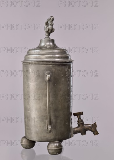 Watering can of the carpenters' guild, guild emblem, probably Warsaw, Poland, cylindrical, supported by three balls, a brass tap with a valve mounted in the lower part; on the sides two rectangular, broken, slightly profiled handles; closed watering can with a profiled, arched lid, topped with a plastic mermaid figurine; on the mantle, above the tap, engraved emblem of the carpenters' guild under a crown, enclosed in a plant wreath, below the inscription: Boguslaw Neuman Beysicz Meyster / Tomasz Prokulski Beysicz Meyster / Bartlomie Baxalarowicz the elder Towrz: / Franz Friser Podstarszy / Antony Jaszesky Podskarby / Anno 1821, dated 1821; vessel, guild memorabilia; height 50.5 cm, width 31.5 cm, depth 29 cm., A tall cylindrical metal container with a domed lid topped by a small sculpted figure, standing on three rounded ball feet, with a vertical handle-like strip on its side and a protruding spout with a valve near the base; visible colors include shades of gray, silver, bronze, and ...