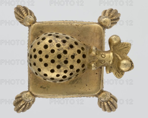Toothpick holder, creator, hedgehog form with tassels on the corners, depicting hedgehogs/animals; on a pad; 2nd quarter of the 19th century; Poland, possibly Warsaw; varia; height 3 cm, width 4.3 cm, depth 4.7 cm, A metallic object with a square base and a domed, perforated rounded piece mounted on top, shown against a pale background; the object has decorative rounded feet at each corner that resemble twisted, rope-like shells and a sculpted protrusion on one side that looks like a stylized head with petal-like elements, all surfaces showing varied wear and patina; the visible colors are gold tones with darker spots and shadowed areas and a light gray background.