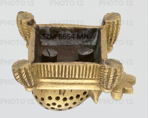 Toothpick holder, hedgehogs, animals, tassels; in the form of a hedgehog on a pad with tassels on the corners; 2nd quarter of the 19th century; Poland, possibly Warsaw; varia; height 3 cm, width 4.3 cm, depth 4.7 cm, A small metallic object with a shiny gold surface showing sculpted ridges and rounded textured elements, including a domed section with multiple circular perforations and a flat rectangular cavity at the top containing two dark cylindrical pieces; the gold surface shows wear and slight discoloration, and the background is a pale light gray.