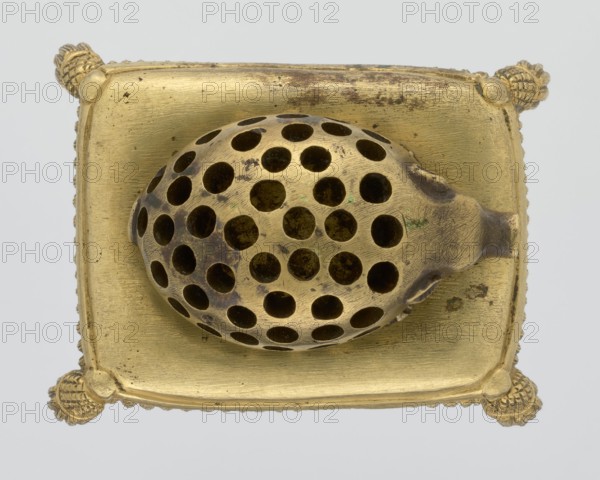 Toothpick holder, purchase provenance noted, hedgehogs, animals, tassels; bronze toothpick holder in the shape of a pig resting on a rectangular base bordered with a fringe; 1820s–1840s; Poland ; varia; height 3.5 cm, width 6.3 cm, depth 4.7 cm., A metallic object with a golden color rests on a square golden base with rounded corners and decorative knobs at each corner; on top of the base sits an oval, perforated dome with many circular holes, also golden but showing darker brownish areas and spots of greenish discoloration; the base surface shows fine scratches and areas of darker tarnish against the overall pale gold background, and the image background is a light gray.