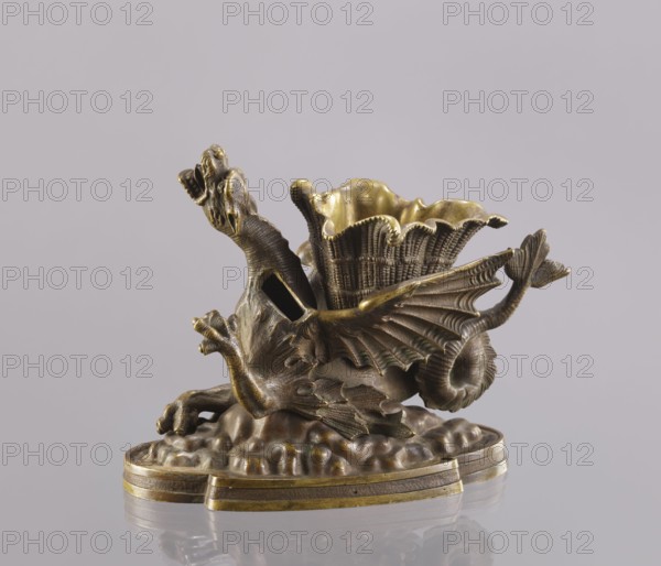 Spirit lamp in the form of a two-winged dragon on a four-leaf oval base. Between the wings is a container; the mouth holds a hole for the wick and a side hole for pouring spirit. According to a catalogue entry, it is an oil lamp and a very old one. Because of the relatively large distance from the bottom of the container to the mouth, the burner could not be fired with oil which has poor capillarity; most likely the lamp was fired with spirit, and the container between the wings was used to hold cigarettes. 2nd half of the 19th century, Polesie. Materials: bronze. Dimensions: height 15.4 cm, width 20.8 cm, depth 10.5 cm. Maker: Roman Szewczykowski 1849–1901 attributed/unknown role., A sculpted metal object resembling a fantastical creature with a dragon-like head, open mouth, textured body, and a pair of ribbed wings, positioned on an irregular, cloud-like base; a flared, scalloped cup with a woven texture rises from the creature's back. The piece displays metallic tones of brown, bron...