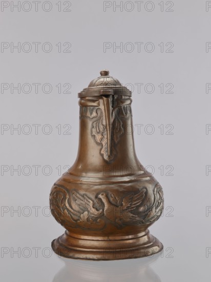 Jug. On a circular, stepped base, the body bulges in the lower part, decorated with a repoussé leafy twig and, at the rim, an eagle with spread wings. Above the two stepped areas is a neck with a spout. Repoussé leaves under the rim and along the rim. The hemispherical handle, fastened with rivets; the lid is hinged with a finger grip, arched, decorated with a leafy rosette and topped with a ball. Maker: Roman Szewczykowski 1849–1901. 1st half of the 18th century. Poland. Vessel. Height 39.5 cm, width 23.9 cm, depth 28.4 cm., A single metal pitcher with a domed lid and a small finial sits against a plain light gray background, showing a warm brown and bronze surface with darker patina in recessed areas. The vessel has a bulbous lower body that tapers into a narrower neck and a flared base, with decorative raised relief carving around the midsection depicting a bird with outstretched wings amid stylized foliage and scrolling motifs. The neck and upper shoulder feature leaf-like relief p...