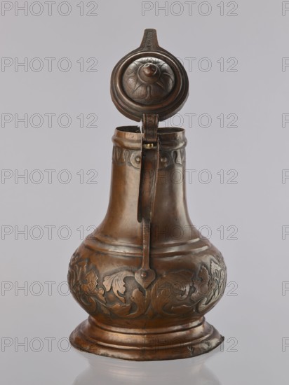 Jug. On a circular, stepped base, the body bulges in the lower part, decorated with a repoussé leafy twig and, at the rim, an eagle with spread wings. Above the two stepped areas is a neck with a spout. Repoussé leaves under the rim and along the rim. The hemispherical handle is fastened with rivets; the lid is hinged with a finger grip, arched, decorated with a leafy rosette and topped with a ball. Maker: Roman Szewczykowski 1849–1901 attributed/unknown role. 1st half of the 18th century, Poland. Vessel. Height 39.5 cm; width 23.9 cm; depth 28.4 cm., A metal pitcher with a hinged lid is shown against a plain light gray background; the pitcher has a rounded base that tapers into a narrow neck with a handle running from the lid to the body. The surface of the pitcher is a warm brownish-bronze with darker brown areas and subtle greenish patina in places, and it features raised decorative floral and foliate patterns around the bulbous midsection and a band of simple ornament near the top....