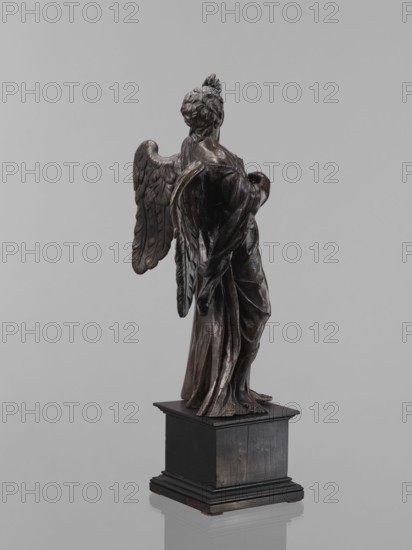Statue - Angel, Renaissance, 16th century. Figure of a standing angel with his left hand raised, the other raised to chest height, which originally held a cross or an element of the Arma Christi. Square wooden base with profiles on the upper and lower edges. Sculpture; height 44 cm, width 12 cm, depth 12.5 cm., A dark brown sculpture of a winged figure stands on a black rectangular pedestal against a light gray background, showing the figure from behind with detailed carved wings, draped flowing garments, and textured hair; the sculpture has glossy and matte surfaces with highlights and shadows, and the pedestal appears solid and slightly worn with visible wood grain.