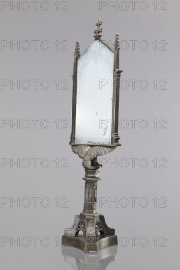 Candle screen. On a three-sided plinth, on a tripod decorated with oak branches, with a hexagonal shaft decorated with pointed-arch arcades containing figures of angels in armor with lances and swords. On the shaft is a figure of an eagle with outstretched wings supporting the frame. Rectangular frame with side pillars decorated with two angels with shields featuring the Prussian eagle, an angel with a banner, and a fourth with an oak branch. Topped with pinnacles bearing angels with olive branches. Triangular closure with openwork tracery and topped with a finial. The frame is fitted with secondary frosted glass. Neo-Gothic composition uses figures from the monument to the wars of 1813–1815, designed by Schinkel, built 1818–1821 and erected in Kreuzberg near Berlin; the figures were made by Friedrich Tieck, Ludwig Wilhelm Wichmann, and Christian Daniel Rauch. Variants of New Year's plaques with views or figures from the monument were produced in the 1820s–1823. Likely 1820s, Germany R...
