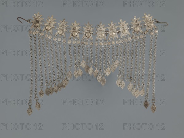 Necklace, 19th century, Middle East, Islamic art; pendants, body and garment ornament, female ornaments; geometric ornament, buttons; fashion accessory; materials: jewelry; height 22.0 cm, width 18.0 cm, weight 131 g., A decorative metal fringe composed of a horizontal row of ornate connectors with textured surfaces and clear reflective elements, from which a group of dangling chains hang, each chain ending in a small leaf-shaped metal pendant with filigree cutouts; the piece is primarily metallic silver with hints of darker patina, set against a flat muted blue-gray background.