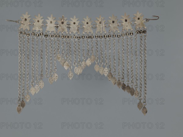 Necklace, 19th century, Middle East, Islamic art; pendants, body and garment ornament, female ornament; geometric ornament, buttons ornament, fashion accessory; jewelry; height 22.0 cm, width 18.0 cm, weight 131 g, A metallic decorative piece with a row of leaf-shaped plates along the top connected by small rings, from which hang a group of chain strands of varying lengths ending in small pierced leaf-shaped pendants; the metal appears silvery with areas of darker patina and spots of brownish discoloration, all set against a smooth muted gray background.