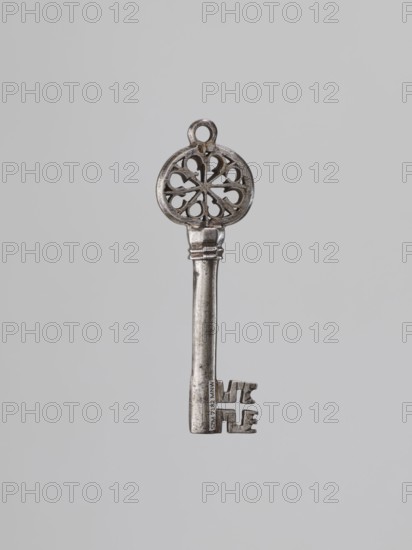 Key, Venetian key; tubular smooth base, blade with a cross-shaped cutout and edge notches. Two rings and an expanded octagonal element. Circular handle with an eight-pointed rosette inscribed inside; between the rays at the bottom are soldered plates forming unclosed circles. Copper soldering. 16th century. Locksmithing, key. Height 10.6 cm; width 3.4 cm; depth 1.3 cm., A single metallic key is centered against a plain light gray background, showing a round ornate bow with a circular opening at the top and a decorative cutout pattern resembling curved petal shapes, a long cylindrical shaft with a slightly wider collar and subtle ridged detailing, and a toothed bit at the end with an irregular stepped profile; the visible colors are silver, gray, and hints of darker tarnished tones.