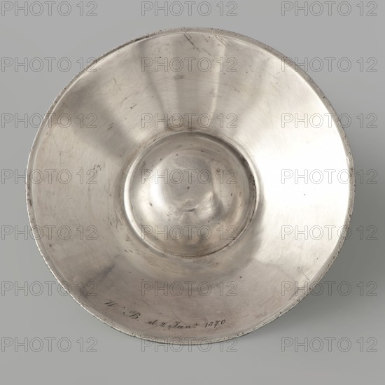 Wine testing bowl, maker Charles-Louis Segay fl. ca 1783, goldsmith. Wine testing vessel shaped characteristic of the Bordeaux region, without a handle, smooth. Engraved inscription under the rim on the outside: Ms WILCKLER A ALTONA FAIT A BORDEAUX CE PREMIER AVRIL 1783. Date: 1783. Place of origin: Bordeaux, France. Vessel; height 2.6 cm, width 11.0 cm., A circular metallic bowl with a shallow, rounded center sits against a smooth pale gray background; the bowl's surface shows a reflective silver tone with areas of darker gray patina and lighter highlights, visible scratches and small blemishes across the interior, and a slightly worn rim with uneven texture.