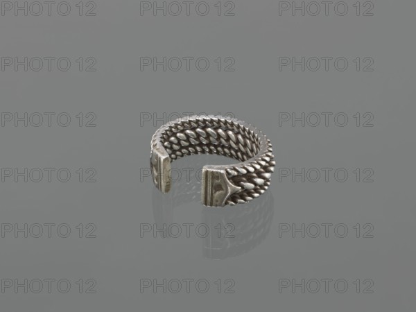 Bracelet, 19th century, Middle East, Islamic art; body/female/hand ornament, fashion accessory; tugra motif; materials: jewelry; dimensions: height 2.5 cm, width 7.0 cm, weight 170 g., A metallic open ring with a woven, braided texture forming its band, displaying a silvery-gray sheen and darker gray shadows, with two flattened end pieces that are slightly worn and show a variation of dull silver and gray tones against a uniform mid-gray background.
