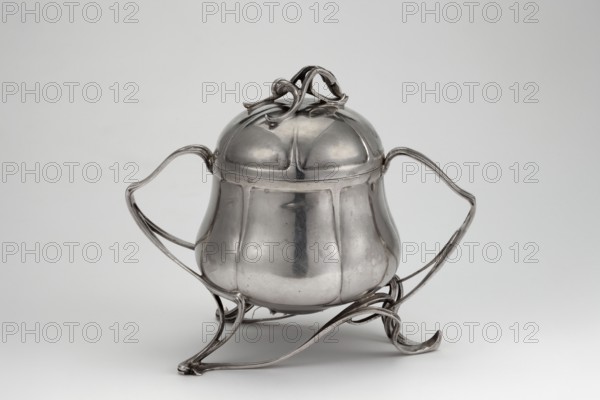 Art Nouveau sugar bowl, Art Nouveau style, plant twig motif, sugar vessel gilded inside, circular with an arched lid with a handle in the form of branches. Large twig-shaped handles extend into three tall supports of the body. Dated 1899–1907. Place of origin uncertain: Germany or Austria. Weight 410 g, height 15 cm, width 18 cm., A polished metal container with a rounded, bulbous body and a domed lid topped by an ornate looping handle sits on an elegant openwork stand; the container has two sweeping curved handles on opposite sides and the stand features sinuous, ribbon-like supports that curl at the ends. The surface is reflective and smooth with visible panels and subtle seams, showing highlights and soft shadows. The visible colors in the image are shades of silver and gray against a light gray background.