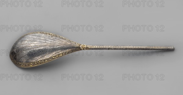 Baroque spoon, baroque style, plant ornament, pearling, cutlery. Baroque spoon with a teardrop-shaped scoop, broken along the axis, gilded inside, the top decorated with a niello ornament of plant tendrils in radial reserves; angular handle decorated with scales, pearling and small leaves. Late 17th century, Poland. Height 23 cm, width 5 cm., A single ornate spoon lies on a plain background, showing a large, scalloped bowl with raised ridges and intricate engraved floral and curvilinear patterns; the bowl has a decorative border with a gold-toned color while the main surface appears silvery with darker shaded areas. The handle is long, narrow, and straight with a beaded or dotted raised pattern along its length and a small decorative collar where it meets the bowl; the handle shows silvery tones with subtle gold accents near the junction. The background is a uniform light gray.