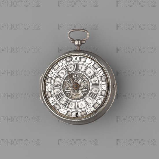 Pocket watch by Isaac Angot fl. ca. 1698–1723. Smooth hemispherical case; silver dial with Roman hour numerals separated by finials and Arabic minute numerals in the reserves; central panoply inscribed ZAMOSC. No minute hand. Bracelet with tendril motif and matching overlays; silver regulator dial; gilded plate surface. Movement: spindle escapement, fusee with chain, four extended pillars with stylized leaf motifs at the top. Baroque style, circa 1710–1723. Timepiece. Height 7.3 cm; width 6 cm. Origin: Zamosc, Poland., A circular metal pocket watch with a hinged loop at the top sits against a solid grey background. The watch face shows ornate concentric rings with raised decorative motifs and radial divisions; its surface appears metallic with areas of darker tarnish and brighter silver highlights. A central raised emblem features sculpted floral and geometric details in darker and lighter silver tones, and a pair of thin metal hands extend outward from the center. The outer rim and ca...