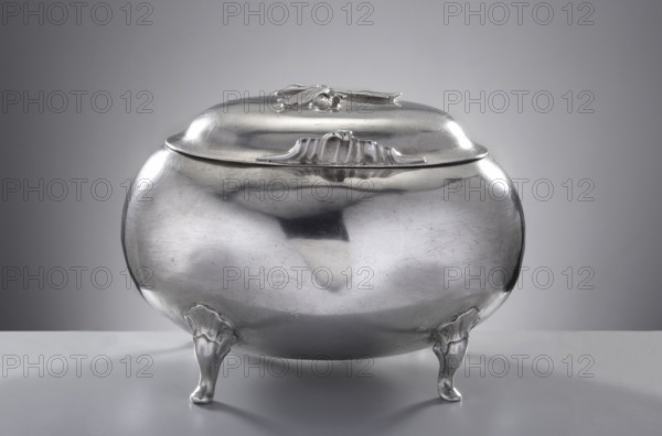 Rococo sugar bowl by Johann Jacob Haase II active from 1759, died 1775, rococo style, egg-shaped sugar bowl on four curved legs decorated with a rooster's comb, with a hinged arched lid, a decorative rocaille handle at the front, topped with a plastic branch flower missing. The sugar bowl is signed twice — with the name of Johann Jacob Haase I and the monogram of Alexander Friedrich Krätzmer Kretschmer. The hallmark of Ende I guild elder in 1770 and 1774 combined with the city mark from 1766–1770 dates the piece to about 1770. The author was probably Johann Jacob d. 1775; Krätzmer may have taken over some unsold production after his death. 1770. Royal Prussia, Gdansk, Poland. Vessel; weight 410 g; height 10.5 cm; width 14 cm; depth 10 cm., A rounded metallic container with a smooth reflective surface sits on a flat surface, supported by a few sculpted legs with ornamental tops; the container has a domed lid with a small decorative element on top and a subtle raised decorative ridge alo...