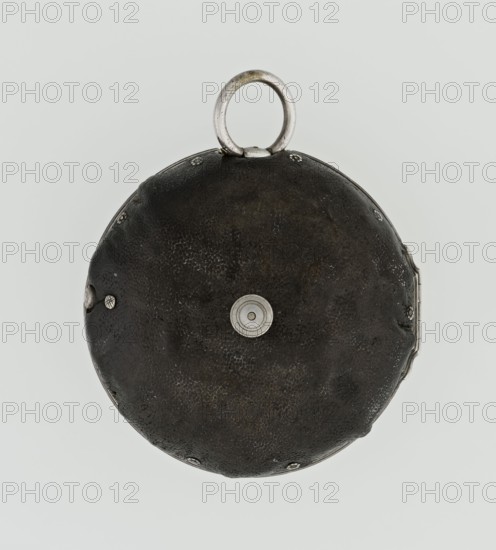 Pocket watch by John Bushman 1692–1720. Silver pocket watch in three cases: outer case covered with leather, rim decorated with studded silver rosettes; middle and inner cases plain. Underside of inner case stamped with casemaker's initial H and number 3081. Transparent lid. Silver champlevé dial with Roman numeral hour markers and Arabic minute markers in oval reserves on a matte background; central circular reserve with the watchmaker's signature on two semicircular plates reading BUSHMAN and LONDON; date window at the bottom. Steel hands with openwork hour hand. Movement with plate skeleton, spring drive, worm gear, and Gall chain; spindle escapement. Gilded lower plate with an openwork English-style bun in the form of a wreath filled with acanthus tendrils and an openwork grid, connected by a mascaron mask with an openwork bun foot. Hair adjustment is a rotating silver-plated dial with scale I–VI. Engraved on the plate in italics: Jn Bushman 3081 / LONDON. Circa 1700, London, Engla...