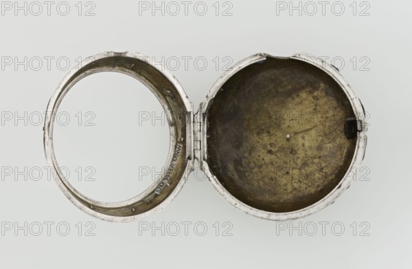 Pocket watch by John Bushman 1692–1720. Silver pocket watch in three cases: outer case covered with leather, rim decorated with studded silver rosettes, middle and inner cases plain; underside of the inner case stamped with the casemaker's initial H and the number 3081; transparent lid. Silver champlevé dial with Roman numeral hour markers and Arabic minute markers in oval reserves on a matte background; central circular reserve with the watchmaker's signature on two semicircular plates reading BUSHMAN and LONDON; date window at the bottom. Steel hands with openwork hour hand. Movement with plate skeleton, spring drive, worm gear, and Gall chain; spindle escapement. Gilded lower plate with an openwork English-style bun in the form of a wreath filled with acanthus tendrils and an openwork grid, connected by a mascaron mask with an openwork bun foot. Hair adjustment via a rotating silver-plated dial with a scale I–VI. Engraved on the plate in italics: Jn Bushman 3081 / LONDON. Circa 1700...