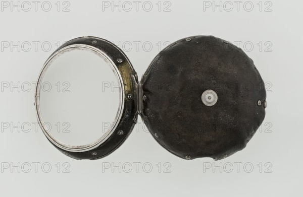 Pocket watch by John Bushman 1692–1720. Silver pocket watch in three cases: outer case covered with leather, rim decorated with studded silver rosettes; middle and inner cases plain. Underside of inner case engraved with casemaker's initial H and number 3081; transparent lid. Silver champlevé dial with Roman numeral hour markers and Arabic minute markers in oval reserves on a matte background; central circular reserve with the watchmaker's signature in two semicircular plates reading BUSHMAN and LONDON; date window at the bottom. Steel hands, openwork hour hand. Movement with plate skeleton, spring drive, worm gear, and Gall chain; spindle escapement. Gilded lower plate with an openwork English-style bun in the form of a wreath filled with acanthus tendrils and an openwork grid, connected by a mascaron mask with an openwork bun foot. Hair adjustment is a rotating silver-plated dial with scale I–VI. Engraved on the plate in italics: Jn Bushman 3081 / LONDON. Circa 1700, London, England....