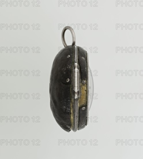 Pocket watch by John Bushman 1692–1720. Silver pocket watch in three cases: outer case covered with leather, decorated on the rim with studded silver rosettes; middle and inner cases plain. Underside of the inner case engraved with the casemaker's initial H and the number 3081. Transparent lid. Silver champlevé dial with Roman numeral hour markers and Arabic minute markers in oval reserves on a matte background; central circular reserve with the watchmaker's signature on two semicircular plates reading BUSHMAN and LONDON; date window at the bottom. Steel hands with openwork hour hand. Movement with a plate skeleton, spring drive, worm gear, and Gall chain; spindle escapement. Gilded lower plate with an openwork English-style bun in the form of a wreath filled with acanthus tendrils and an openwork grid, connected by a mascaron mask with an openwork bun foot. Hair adjustment via a rotating silver-plated dial with scale I–VI. Engraved on the plate in italics: Jn Bushman 3081 / LONDON. Ci...