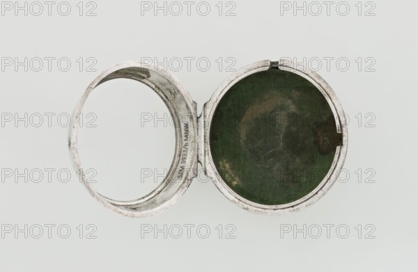 Pocket watch by John Bushman 1692–1720. Silver pocket watch in three cases: outer case covered with leather, rim decorated with studded silver rosettes; middle and inner cases plain. Underside of inner case stamped with casemaker's initial H and number 3081. Transparent lid. Silver champlevé dial with Roman numeral hour markers and Arabic minute markers in oval reserves on a matte background; central circular reserve with the watchmaker's signature on two semicircular plates reading BUSHMAN and LONDON; date window at the bottom. Steel hands with openwork hour hand. Movement with plate skeleton, spring drive, worm gear, and Gall chain; spindle escapement. Gilded lower plate with an openwork English-style bun in the form of a wreath filled with acanthus tendrils and an openwork grid, connected by a mascaron mask with an openwork bun foot. Hair adjustment is a rotating silver-plated dial with a scale I–VI. Engraved on the plate in italics: Jn Bushman 3081 / LONDON. Circa 1700, London, Eng...
