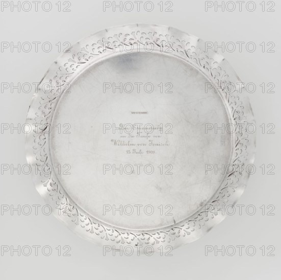 Circular tray, scrap, ca. 1908, England, Birmingham; dish; diameter 32 cm; weight 722 g, A round metal plate with a wide decorative rim featuring a repeating cut-out vine or leaf motif and a smooth central area with visible surface scratches and scuffs; the plate is predominantly silver with a few darker gray marks and slight discolorations, and it is shown against a light gray background.