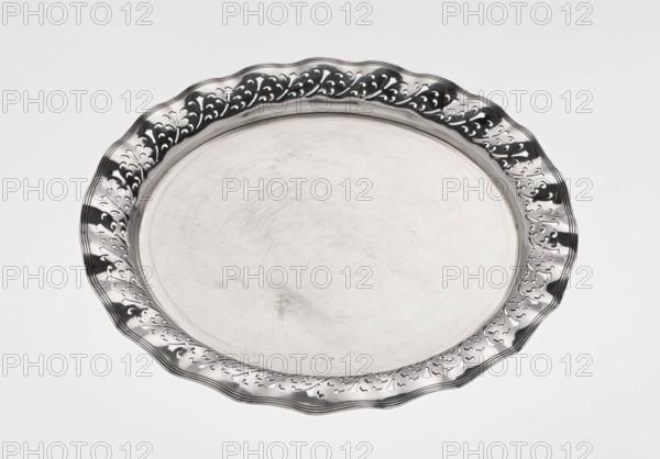 Circular tray, scrap, purchased ca. 1908, England, Birmingham; dish, diameter 32 cm, weight 722 g, A round metal tray with a scalloped rim and decorative cutout pattern around the edge, shown against a light background; the tray surface is smooth with visible scratches and wear, and the metal appears shiny with reflective areas in silver and darker gray tones.