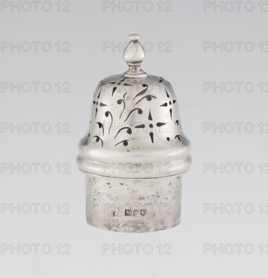 Powdered sugar bowl, maker: Harrod's Stores Ltd; maker/person: Richard Burbidge 1847–1917, goldsmith. Pear-shaped powdered sugar bowl on a circular profiled foot, with a domed openwork cover topped with a bowl. Edge of the foot and the top rim decorated with astargal. Openwork; function: sugar vessel. Dish; height 15 cm, diameter 5.9 cm; weight 152 g. Date: 1913–1914. Place: London, England., The image shows a metallic, bell-shaped object with a rounded finial on top and a domed perforated upper section featuring decorative cutouts, sitting on a cylindrical base that appears worn and slightly tarnished; visible colors include shades of silver, gray, and hints of darker gray in the cutout areas and surface marks.