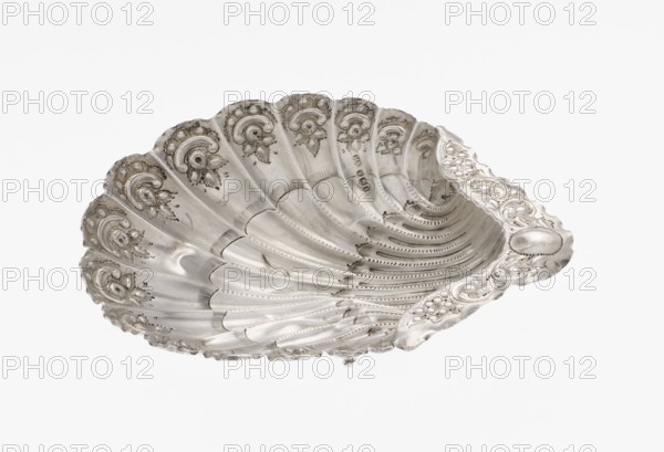 Platter in the form of a shell, Atkin Brothers Silversmith Ltd Sheffield; goldsmith and silversmith firm; 1826–1958 — Silver platter in the form of a full-plastic scallop shell, knotted and ribbed, decorated on the rim with a motif of relief flowers, leaves and channel sections; supported on three shell feet. Floral ornaments; shell shape; knotting; scallop shell. Date: 1890/1891. Place: Sheffield, England, Great Britain. Function: vessel. Dimensions: height 2.5 cm; width 15.3 cm; depth 13.1 cm; weight 113 g. Provenance: scrap — purchase, purchase., A metallic shell-shaped dish with a scalloped rim, displaying ornate raised floral and scrollwork decoration along the edges and interior; the surface shows fine engraved lines, dotted patterns, and textured bands radiating from the center, with areas of smooth polished metal and slight discoloration; overall color is silver with subtle darker gray accents where shadows and detailing appear.