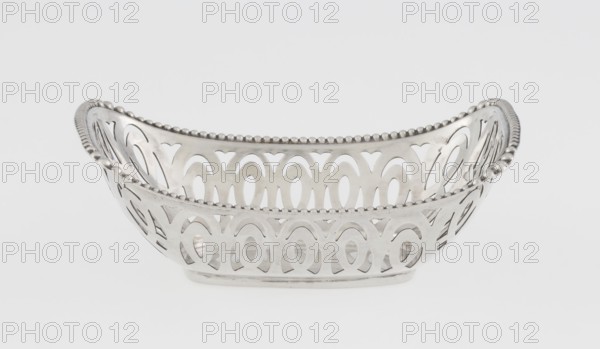 Openwork basket by Steinhart & Co Birmingham, London; goldsmith, merchant; fl. 1897–1930. Openwork silver basket, rectangular with raised edge on the longer axis; edge bordered with pearling ribbon. Openwork forms a composition of elongated ovals and arcades. Decorated with geometric ornaments and pearling. Dated 1910–1911, Birmingham, England. Vessel. Height 7.3 cm, width 9.6 cm, depth 6.7 cm, weight 40 g., A silver-toned decorative bowl with an openwork pattern and scalloped bead trim along the top edge, shown against a plain light gray background; the bowl has a curved, elongated shape with repeating arch and oval cutouts and a reflective metallic surface with highlights and subtle shadows.