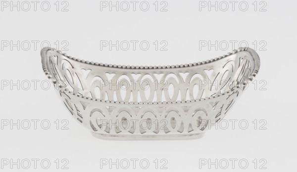 Openwork silver basket, openwork geometric ornaments with pearling; rectangular with raised edge on the longer axis; edge bordered with pearling ribbon; openwork forms a composition of elongated ovals and arcades. Maker: Steinhart & Co Birmingham, London; goldsmith, merchant; fl. 1897–1930. Date: 1910/1911. Place: Birmingham, England, Great Britain. Function: vessel. Dimensions: height 7.3 cm, width 9.6 cm, depth 6.7 cm; weight 40 g., A silver metal basket with an openwork pattern and scalloped bead trim along the top edge sits against a plain light gray background; the basket has a curved rectangular shape with decorative cutouts forming repeating oval and arch shapes, raised sides that slope upward at the ends, and a smooth reflective surface showing highlights and subtle shadows in shades of silver and gray.