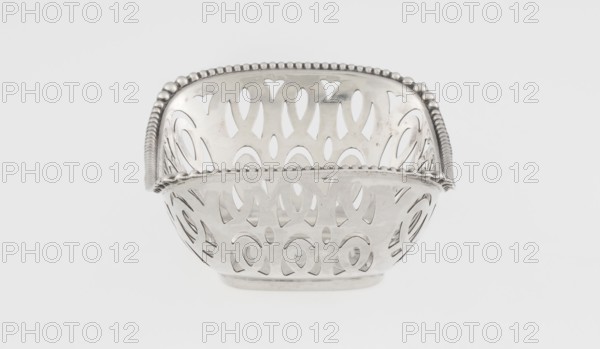 Openwork basket by Steinhart & Co Birmingham, London; goldsmith, merchant; active 1897–1930. Openwork silver rectangular basket with raised edge along the longer axis; edge bordered with pearling ribbon. Openwork forms a composition of elongated ovals and arcades; geometric ornaments and pearling. Dated 1910–1911, made in Birmingham, England. Vessel; height 7.3 cm, width 9.6 cm, depth 6.7 cm, weight 40 g., A metallic bowl with a decorative pierced pattern and a beaded rim sits centered against a plain light background; the bowl appears reflective and silver in color with cutout oval and teardrop shapes around its sides and a scalloped beaded edge, and the background is light gray to white.