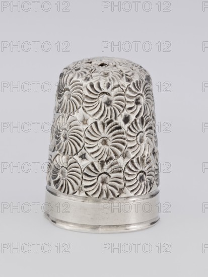 Thimble by James Fenton Birmingham goldsmiths' firm, fl. 1852–1954. Conical silver thimble with a smooth lower edge; upper surface covered with relief decoration of swirling rosettes. Ornament: rosette scrap-purchase. Function: sewing accessory. Dated 1893–1894, Birmingham, England. Height 2.2 cm; diameter 1.5 cm; weight 49 g., A metallic thimble with an embossed floral swirl pattern covering its rounded body, showing a shiny silver color with darker tarnished areas in the recessed parts of the pattern and a smooth silver band at the base, set against a light gray background.