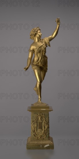 Candlestick, lyre iconographic, swans iconographic, 19th century, Paris, France, lighting, height 54 cm, A gilded bronze statue of a female figure standing on one foot atop an ornate rectangular pedestal, the figure wearing a draped garment with textured detailing and a floral or leafy headpiece, one arm raised upward holding a small object and the other arm extended slightly outward, the figure's hair styled in curls and the body shown in a graceful, balletic pose; the pedestal decorated with sculpted ornamental motifs including a lyre-like central element flanked by symmetrical decorative forms and topped by a stepped plinth, all set against a plain gray background; visible colors include gold tones on the statue and pedestal and shades of gray in the background.