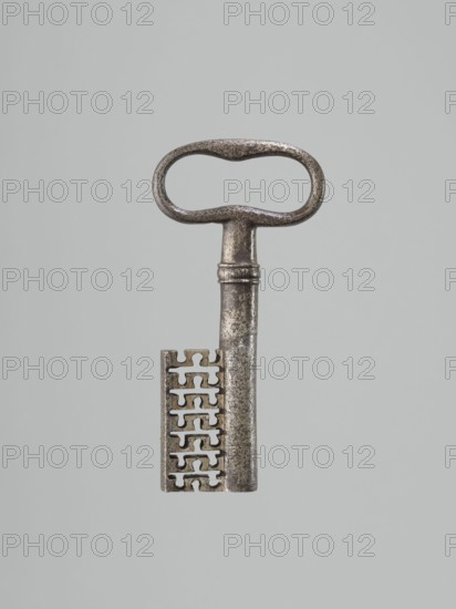 Lock key, locksmithing. One-sided register with a key pin; octagonal plates; bottom side extensions with screw holes; triangular profiled reinforcements on the walls. A rectangular reinforcing strip on the top plate. Key with a tubular, smooth shaft; bow with seven vertical ribs, with two recesses on one side and one on the other. Extended, ending with an arched extension. 18th century, Central Europe; metalwork; height 12 cm, width 5.8 cm, depth 1.6 cm., A single metal key with a rounded, oval handle and a long shaft is centered against a plain light gray background; the key shows a worn, textured surface with a metallic silver-gray color and darker patina in areas, and the bit features a vertical series of interlocking notches creating a patterned edge with visible shadows and highlights in silver and darker gray tones.