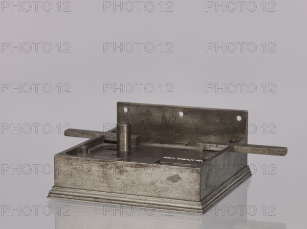 Square-faced lock by Michal Taszynski fl. 1820–1838. Door lock with latches and key, No. 114, made in 1861 and marked with the guild marks of the Warsaw Locksmiths' Assembly. Precisely crafted, it uses protruding side bolts latches to lock the door simultaneously in three directions—top, bottom, and middle. Ornamentation on the top features a light pattern. Mechanism: a resting bolt with two heads and a latch bolt between them that opens with a half-turn; a full turn of the key activates the double bolt and the locking mechanism. Neat workmanship; inside the box, on the side, a hallmark is stamped twice—depicting a striding figure with a large key, likely a striding bear styled like the city's 19th-century coat of arms, indicating the work of a master. Attributed to Michal Daniel Taszynski born 1836, son of Michal Taszynski, a locksmith specializing in polished steel accessories, who purportedly made his masterpiece in 1861. Technique: locksmithing. Dimensions: height 16.1 cm, width 15...
