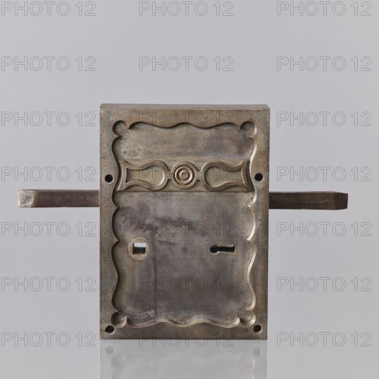 Vault lock by Karol Konstabel, locksmith, 2nd half of the 19th century, Warsaw. Masterpiece marked with the guild stamp stamp now invisible. Cabinetry and workmanship, and the key register, are especially outstanding. The lock has three bolts and a fourth latch bolt connected to the handle handle missing. The rectangular cup has an overlaid border with an inner wavy edge, and a three-length vertical strip with a sequin and two inverted lyre shapes. On the underside, the case with the mechanism is separated, with a narrow chamber that was meant to cover the bolt hasps. Shares the same technical solution as a handmade lock described as Taszynski's from 1861; described in the Crafts Act of 1816 as a precise treasury lock for a main door with flanking riffles with two springing and two lifting fels. Karol Konstabel was probably the son of Wilhelm, a master locksmith recorded by Dzierzanowski. Dimensions: height 40 cm, width 27.5 cm, depth 12.5 cm., A rectangular metal lock plate with a wea...